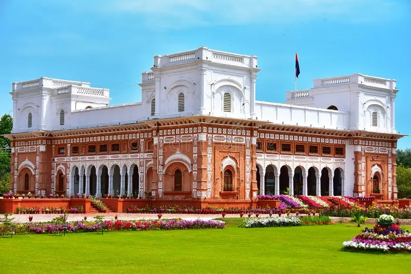 Nishat Mahal palace in Bahawalpur — red brick facade with white stucco accents, Corinthian balustrades, and octagonal towers against a clear sky