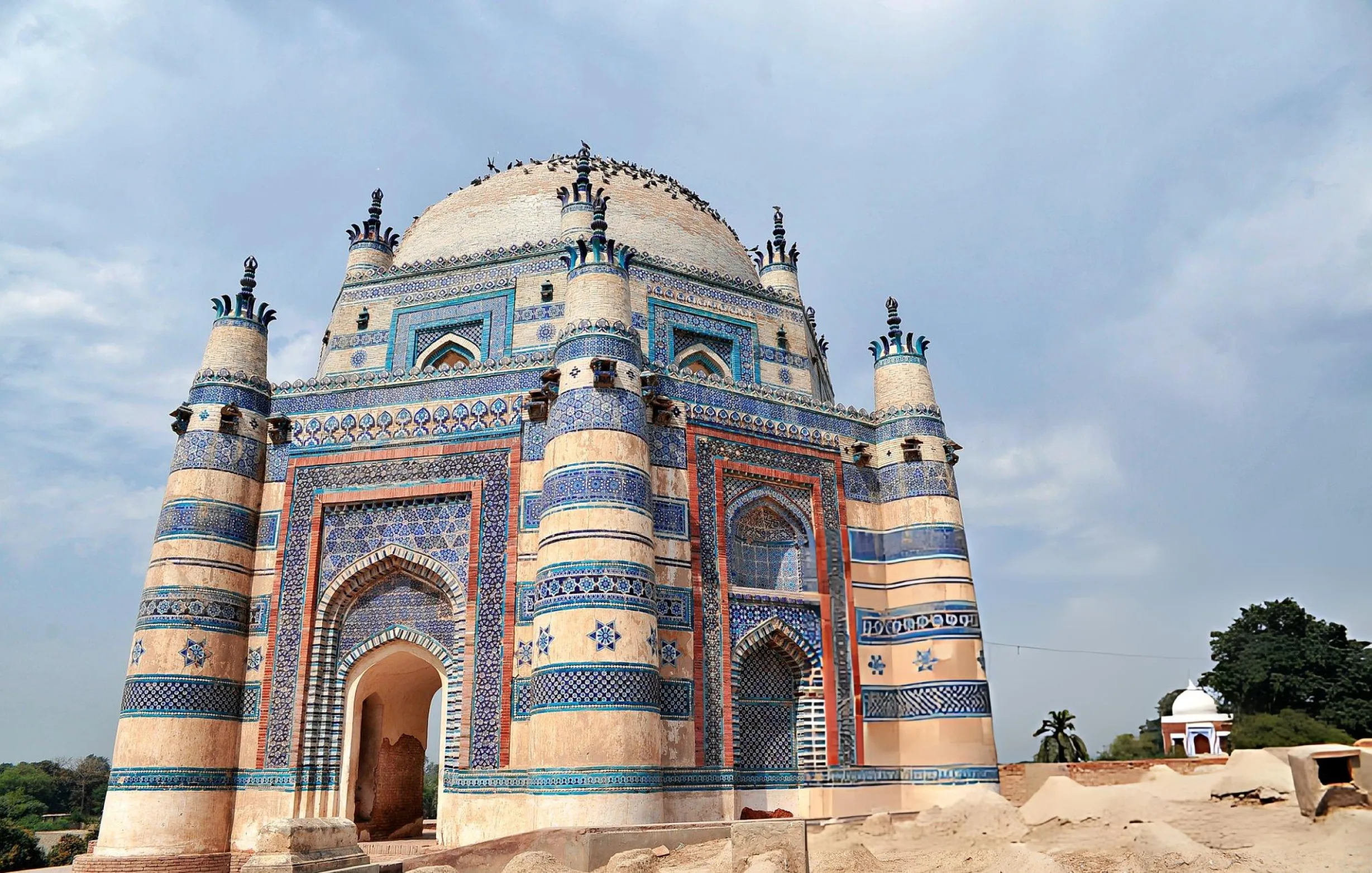Tomb of Bibi Jawindi in Uch Sharif — octagonal half-ruin with blue and white glazed tiles against desert landscape